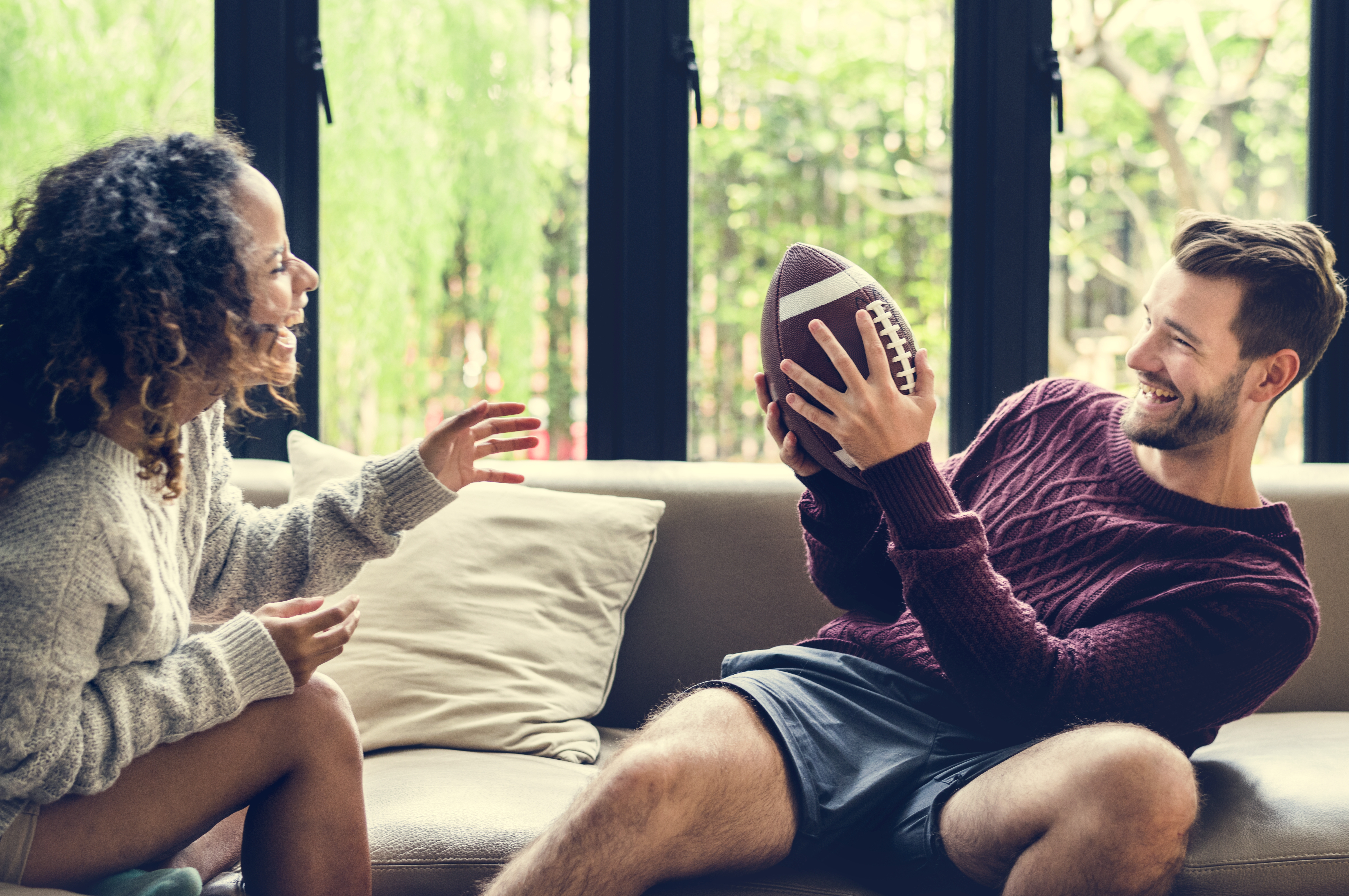 a woman and a man sit on a couch and toss a football back and forth